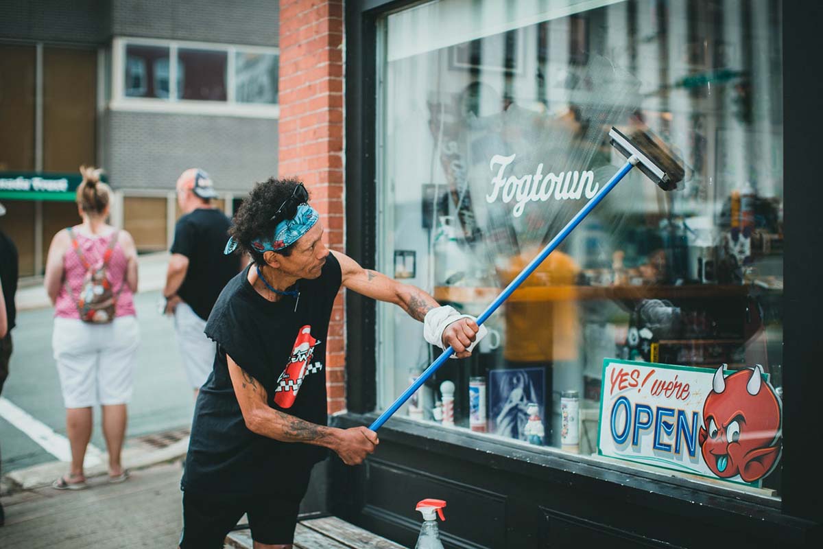 A Man in Black Tank Top Cleaning the Glass Window near the Street